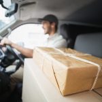 Delivery driver driving van with parcels on seat outside the warehouse