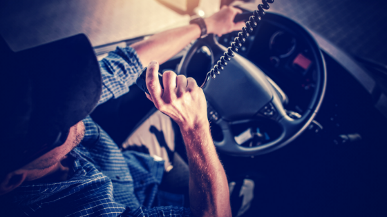 Truck driver is dark blue ball cap and blue plaid shirt talks into a CB Radio