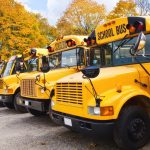 Row of yellow school buses against autumn trees
