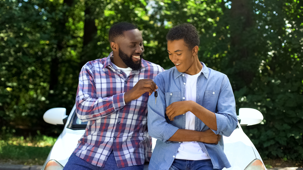 Happy dad giving car key to son, permission to drive, parenthood trust, family